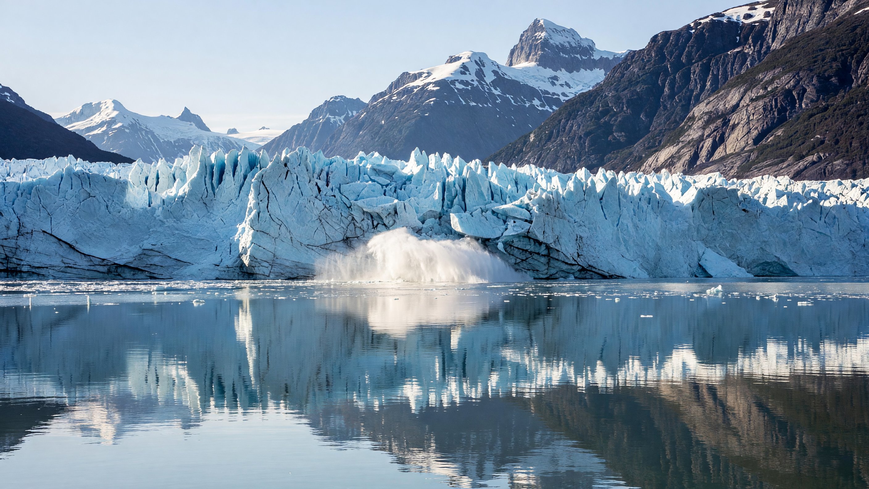 Tidewater glacier calving into Glacier Bay, Alaska, with mountain reflections in calm fjord water