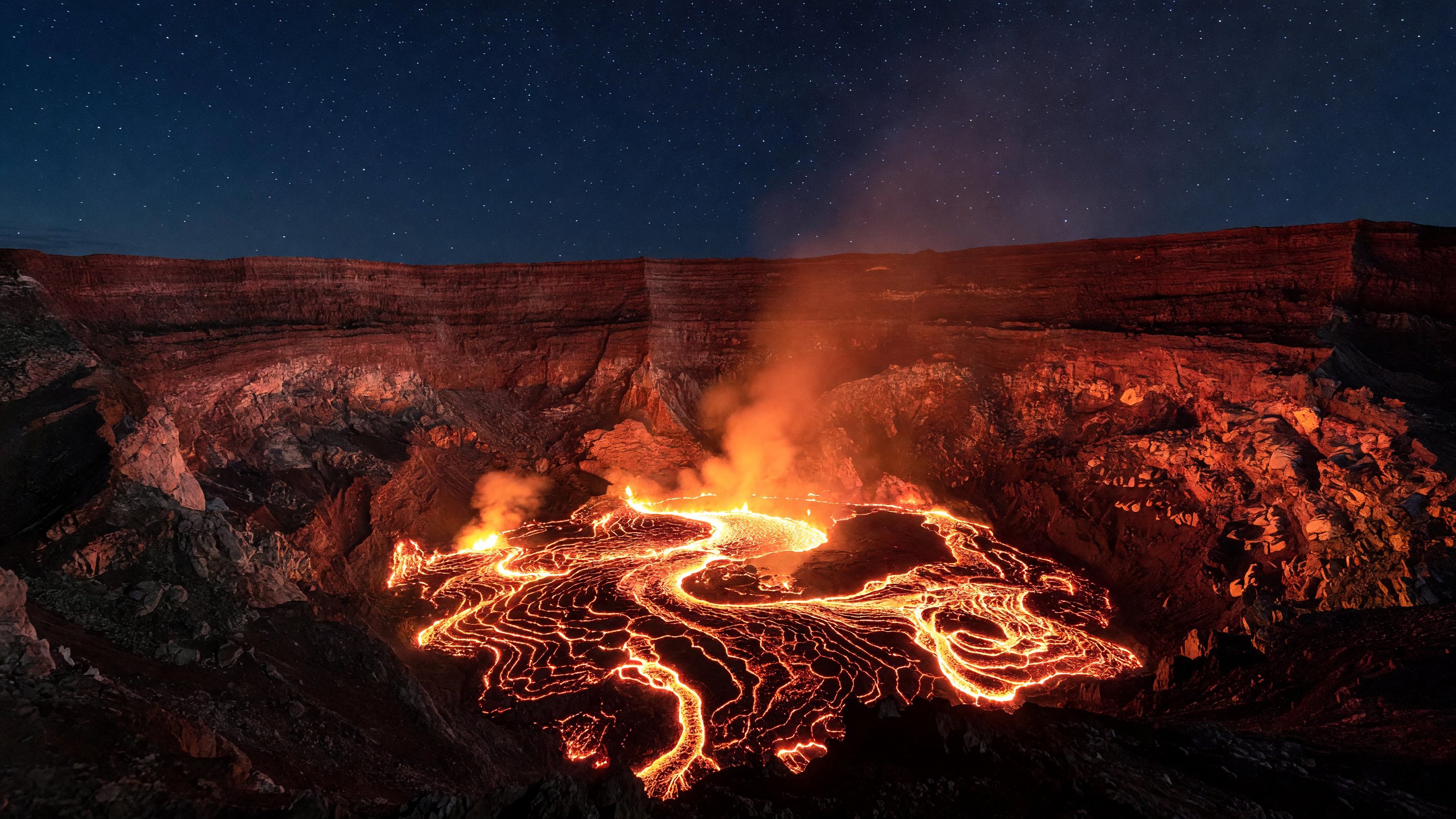 Glowing lava lake inside Halemaʻumaʻu Crater at night, illuminating the caldera walls of Kīlauea in Hawaii Volcanoes National Park